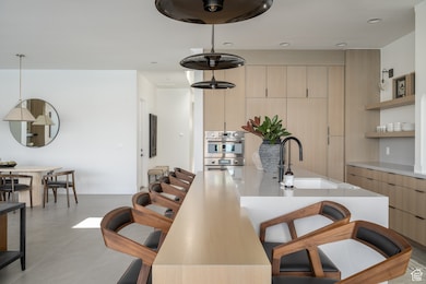 Kitchen featuring a kitchen bar, modern cabinets, light brown cabinets, a sink, and light countertops