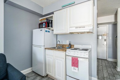 Kitchen with white appliances, wood finish floors, white cabinetry, under cabinet range hood, and a textured ceiling
