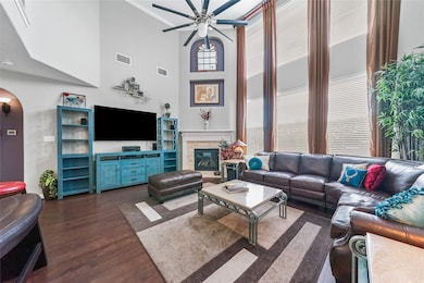 This family gathering area features a fireplace mantel detailing custom paint and ceiling fan, soaring high ceilings, rich engineered flooring with plenty of natural lighting.