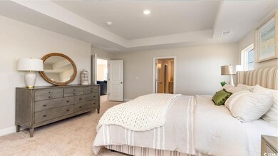 Bedroom with light carpet, a tray ceiling, and ens