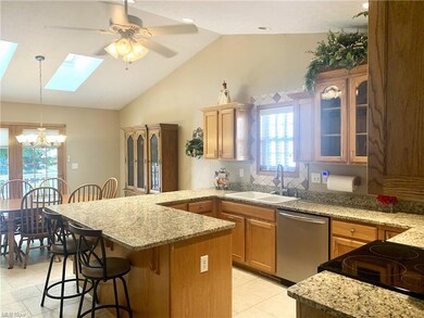 Kitchen with stainless steel dishwasher, decorative light fixtures, lofted ceiling with skylight, electric stovetop, light stone counters, brown cabinets, and light tile floors