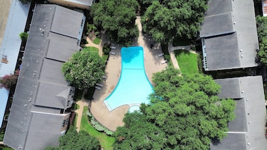This aerial photo showcases a serene residential complex featuring a uniquely shaped swimming pool surrounded by lush greenery and multiple buildings, creating a peaceful and inviting community atmosphere.