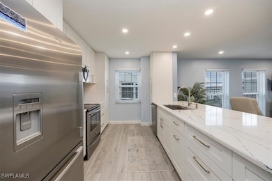 Kitchen featuring appliances with stainless steel finishes, white cabinets, light stone counters, light wood-style flooring, and recessed lighting
