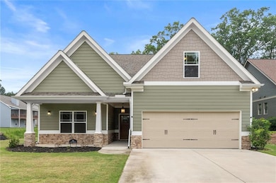 Craftsman-style home with driveway, stone siding, a front yard, a garage, and roof with shingles