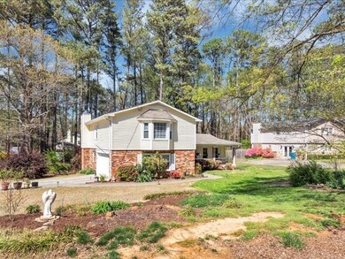 View of side of property featuring driveway, a chimney, an attached garage, brick siding, and a lawn