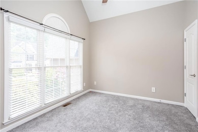 Empty room featuring lofted ceiling, carpet flooring, and a ceiling fan