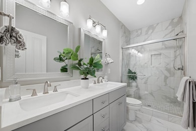 Bathroom featuring a stall shower, double vanity, light marble finish floors, and recessed lighting