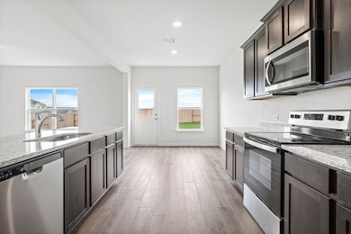 Kitchen featuring stainless steel appliances, light stone countertops, dark brown cabinets, light wood-style flooring, and recessed lighting