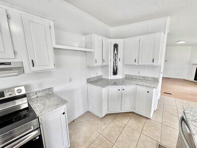 Kitchen with appliances with stainless steel finishes, exhaust hood, white cabinetry, and a textured ceiling