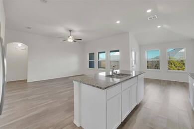 Kitchen with white cabinetry, sink, light stone countertops, vaulted ceiling, and a center island with sink