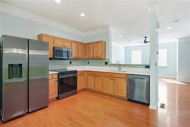 Kitchen featuring stainless steel appliances, a sink, light wood finished floors, ornamental molding, and light countertops