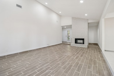 Unfurnished living room with high vaulted ceiling, recessed lighting, a brick fireplace, and wood finish floors