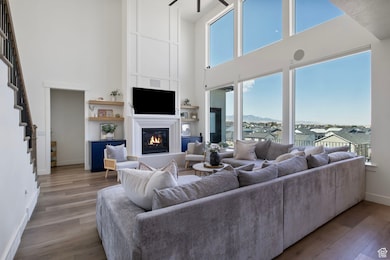 Living area with a towering ceiling, a glass covered fireplace, stairs, and wood finished floors