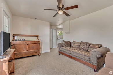 Carpeted living room featuring ceiling fan and baseboards