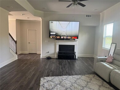 Living room with a fireplace with flush hearth, wood finished floors, ornamental molding, stairway, and a ceiling fan