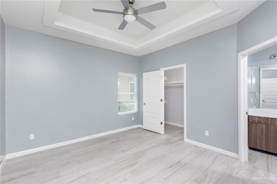 Unfurnished bedroom featuring a raised ceiling, connected bathroom, light wood-type flooring, and a walk in closet