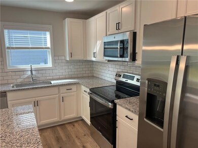 Kitchen with stainless steel appliances, a sink, light wood finished floors, white cabinets, and decorative backsplash