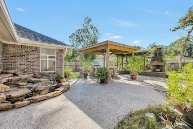 This backyard features a spacious patio with an outdoor seating area, perfect for entertaining. It includes a stone water feature and a built-in fireplace, surrounded by lush greenery for a serene atmosphere.