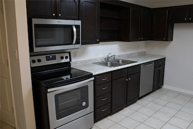 Kitchen with appliances with stainless steel finishes, light tile patterned floors, light countertops, open shelves, and dark brown cabinets