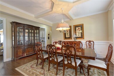 Dining area with dark wood finished floors, ornamental molding, a chandelier, and coffered ceiling