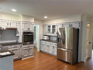 Kitchen with appliances with stainless steel finishes, crown molding, light wood finished floors, decorative backsplash, and glass insert cabinets