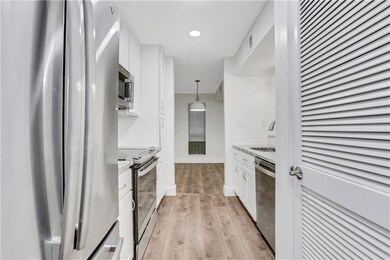 Kitchen with appliances with stainless steel finishes, white cabinets, light wood-style flooring, a sink, and decorative light fixtures
