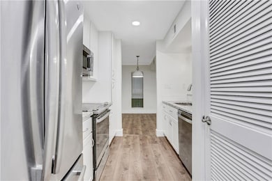 Kitchen with appliances with stainless steel finishes, white cabinets, light wood-style flooring, a sink, and decorative light fixtures