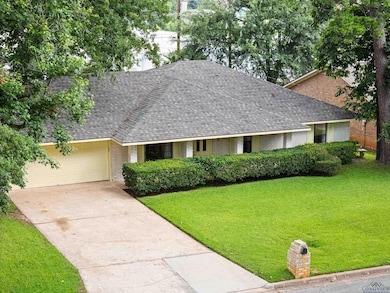 Ranch-style home with brick siding, a shingled roof, a front yard, a garage, and driveway