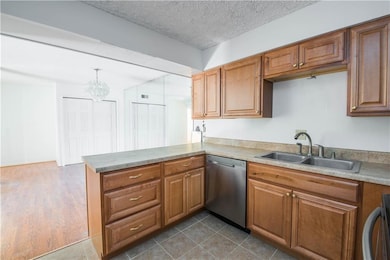 Kitchen with stainless steel dishwasher, a sink, a peninsula, brown cabinetry, and a textured ceiling