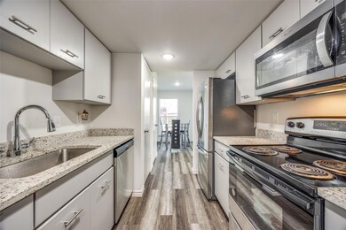 Kitchen with sink, light hardwood / wood-style flooring, appliances with stainless steel finishes, light stone counters, and white cabinetry