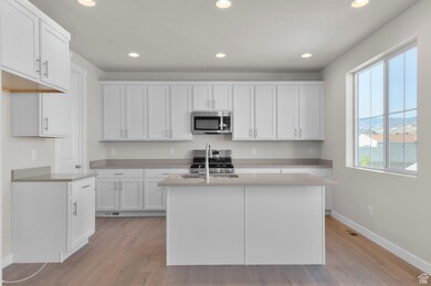 Kitchen featuring recessed lighting, white cabinetry, stainless steel appliances, light wood-type flooring, and a center island with sink