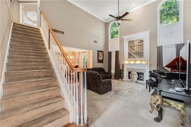 Living room with ornamental molding, a ceiling fan, stairs, a towering ceiling, and carpet flooring