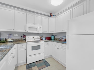 Kitchen with white appliances, white cabinetry, light tile patterned flooring, dark stone counters, and ornamental molding