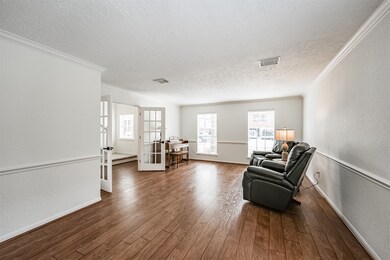 To the left of the foyer, French doors open into this flexible-use combined formal living and dining room that features fresh neutral paint, crown and chair rail molding, a pair of front-facing windows, and continued wood-look laminate floors.