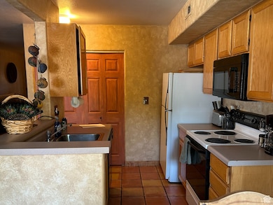 Kitchen featuring electric stove, black microwave, light tile patterned flooring, and a textured ceiling