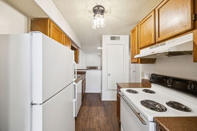 Kitchen featuring white appliances, a textured ceiling, brown cabinetry, under cabinet range hood, and dark wood finished floors