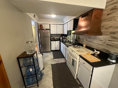 Kitchen featuring freestanding refrigerator, white range with electric cooktop, dark countertops, white cabinetry, and decorative backsplash