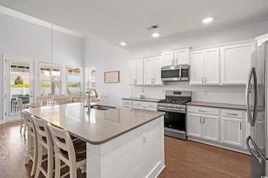 Kitchen with stainless steel appliances, dark wood-style flooring, a chandelier, decorative backsplash, and white cabinets