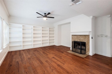 Unfurnished living room featuring a tiled fireplace, a textured ceiling, crown molding, dark wood-style floors, and a ceiling fan
