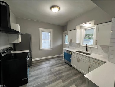 Kitchen with stainless steel dishwasher, backsplash, white cabinets, light countertops, hardwood flooring, and range with electric stovetop
