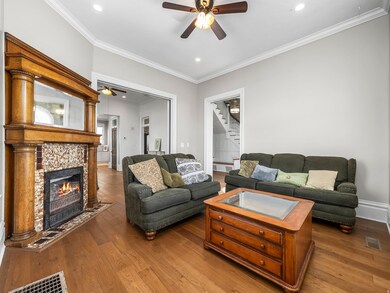 Living area featuring ceiling fan, ornamental molding, dark wood-style floors, stairway, and a fireplace