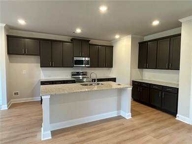 Kitchen featuring appliances with stainless steel finishes, a kitchen island with sink, light stone countertops, light wood finished floors, and ornamental molding