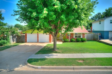 View of property hidden behind natural elements featuring a garage, brick siding, and driveway