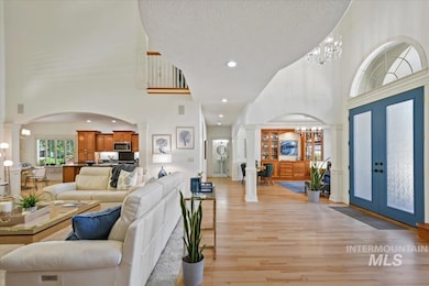 Living area featuring ornate columns, a high ceiling, arched walkways, french doors, and light wood-type flooring