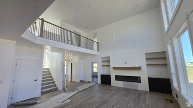 Unfurnished living room featuring a towering ceiling, dark wood-style floors, a glass covered fireplace, and stairway