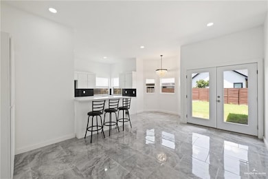 Kitchen featuring a peninsula, white cabinetry, a kitchen bar, french doors, and recessed lighting