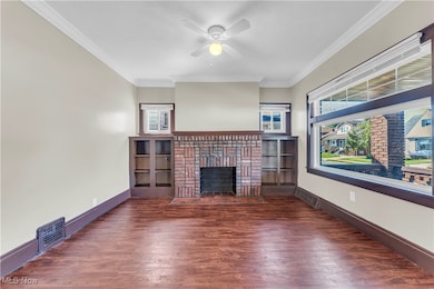 Unfurnished living room featuring crown molding, a brick fireplace, dark wood-type flooring, and a ceiling fan