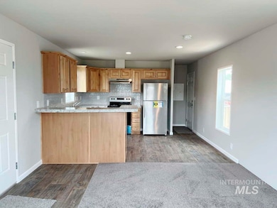 Kitchen featuring appliances with stainless steel finishes, wood finished floors, under cabinet range hood, decorative backsplash, and a peninsula