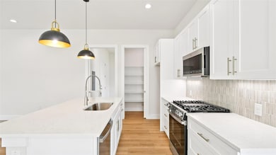Kitchen with light stone counters, appliances with stainless steel finishes, pendant lighting, light wood finished floors, and recessed lighting