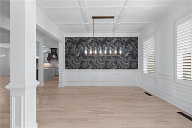 Unfurnished dining area featuring a chandelier, wallpapered walls, coffered ceiling, light wood-type flooring, and wainscoting
